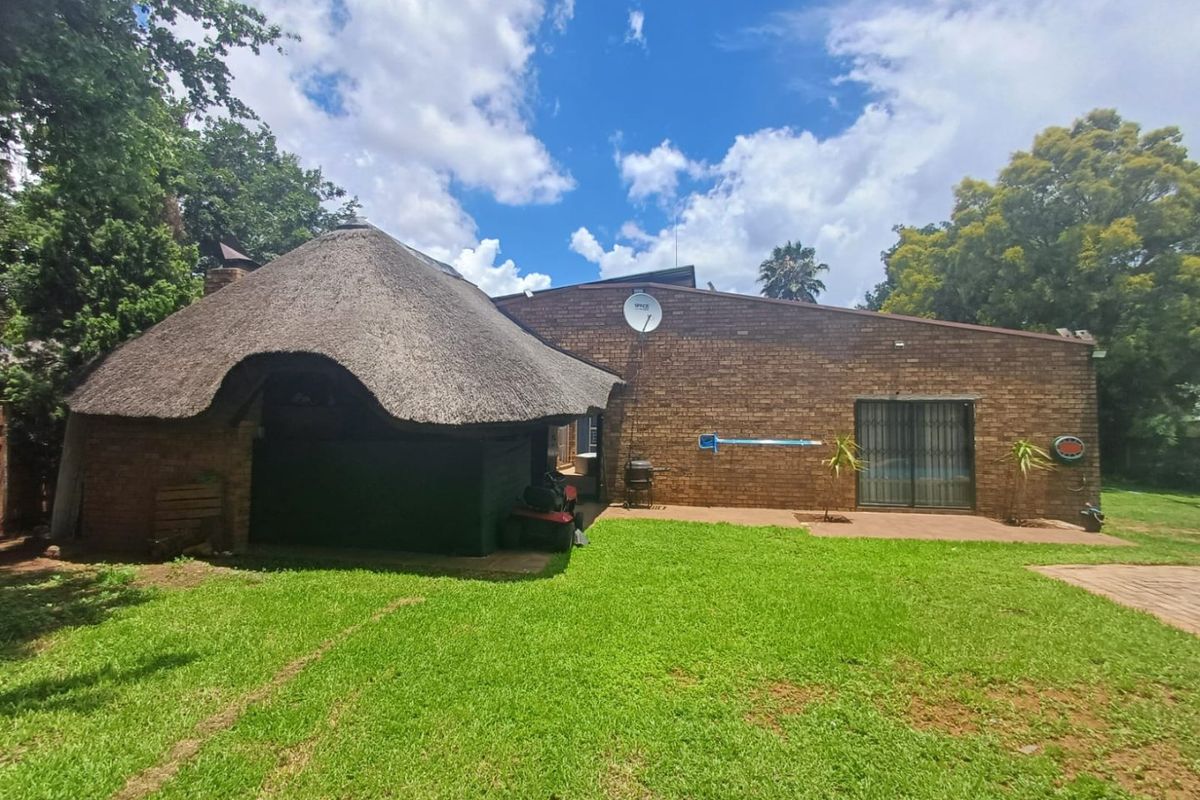 Rear view of the property featuring a brick facade, a traditional thatch roof section, and a spacious garden area.