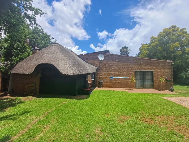 Rear view of the property featuring a brick facade, a traditional thatch roof section, and a spacious garden area.
