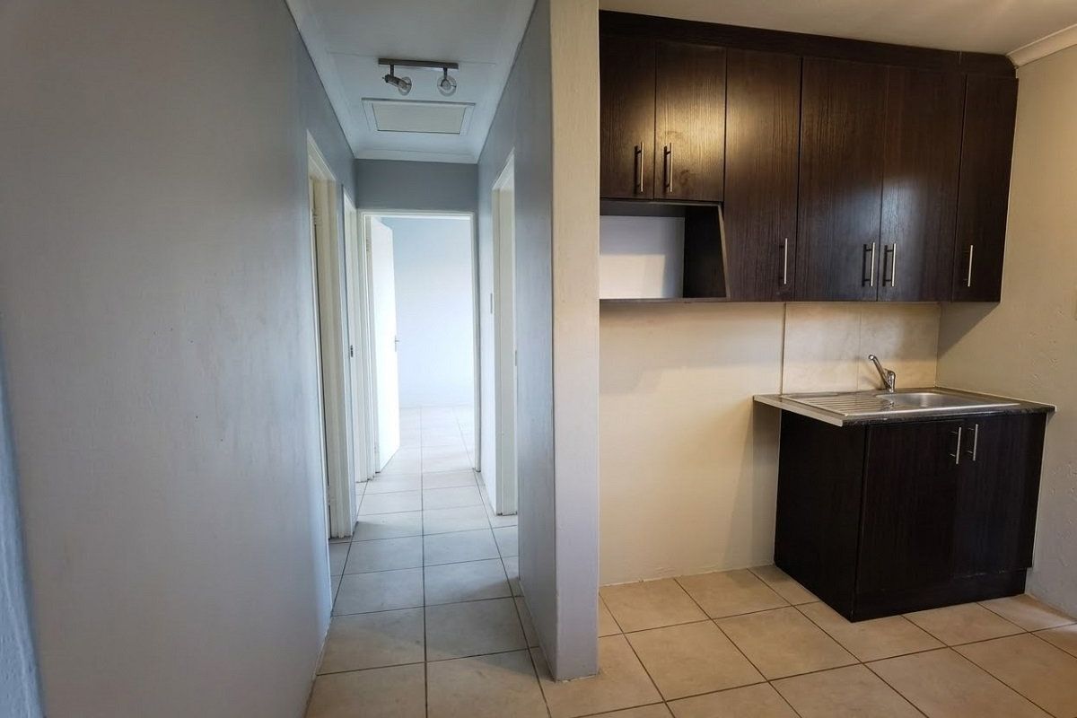 A compact kitchen area featuring dark wood cabinetry and a stainless steel sink, adjacent to a tiled hallway leading to other rooms.