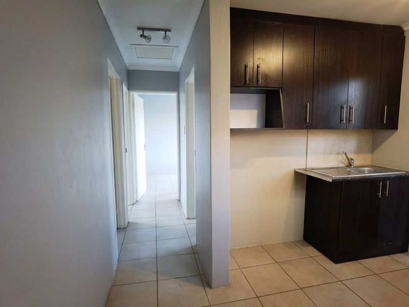 A compact kitchen area featuring dark wood cabinetry and a stainless steel sink, adjacent to a tiled hallway leading to other rooms.
