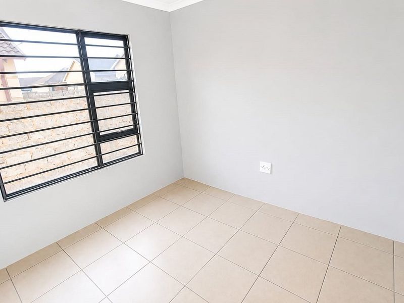 A clean, empty bedroom featuring neutral tiled flooring, light grey walls, and a window fitted with security bars.