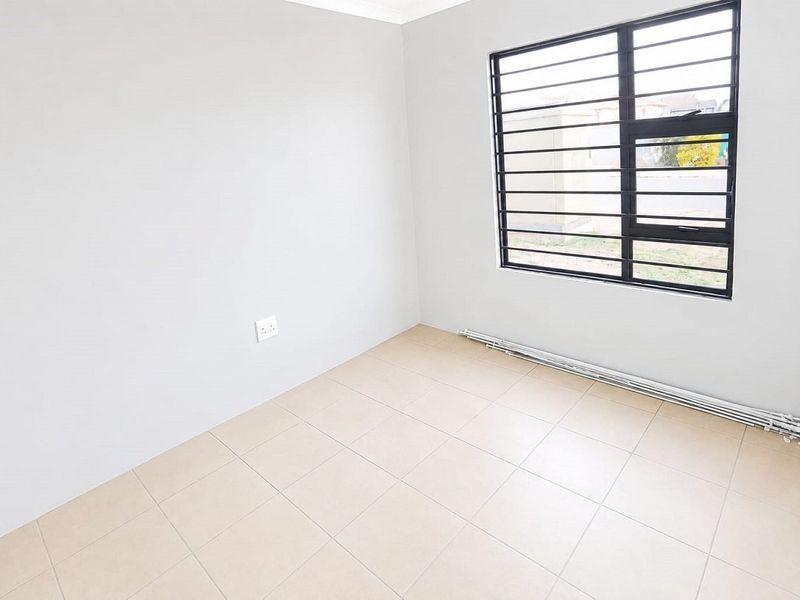 A clean, empty bedroom featuring neutral tiled flooring, light grey walls, and a window fitted with security bars.