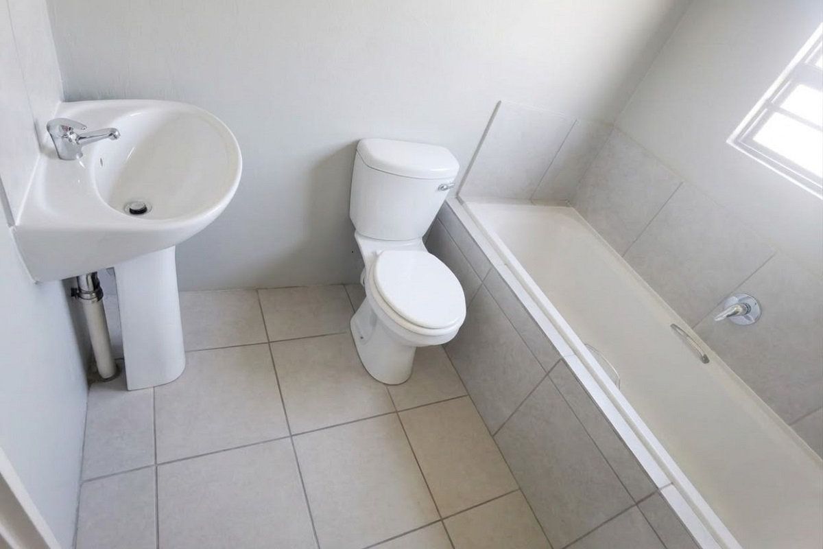 A clean, functional bathroom featuring a pedestal basin, standard toilet, and a bathtub with tiled surround and flooring.