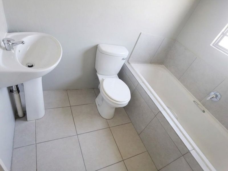 A clean, functional bathroom featuring a pedestal basin, standard toilet, and a bathtub with tiled surround and flooring.