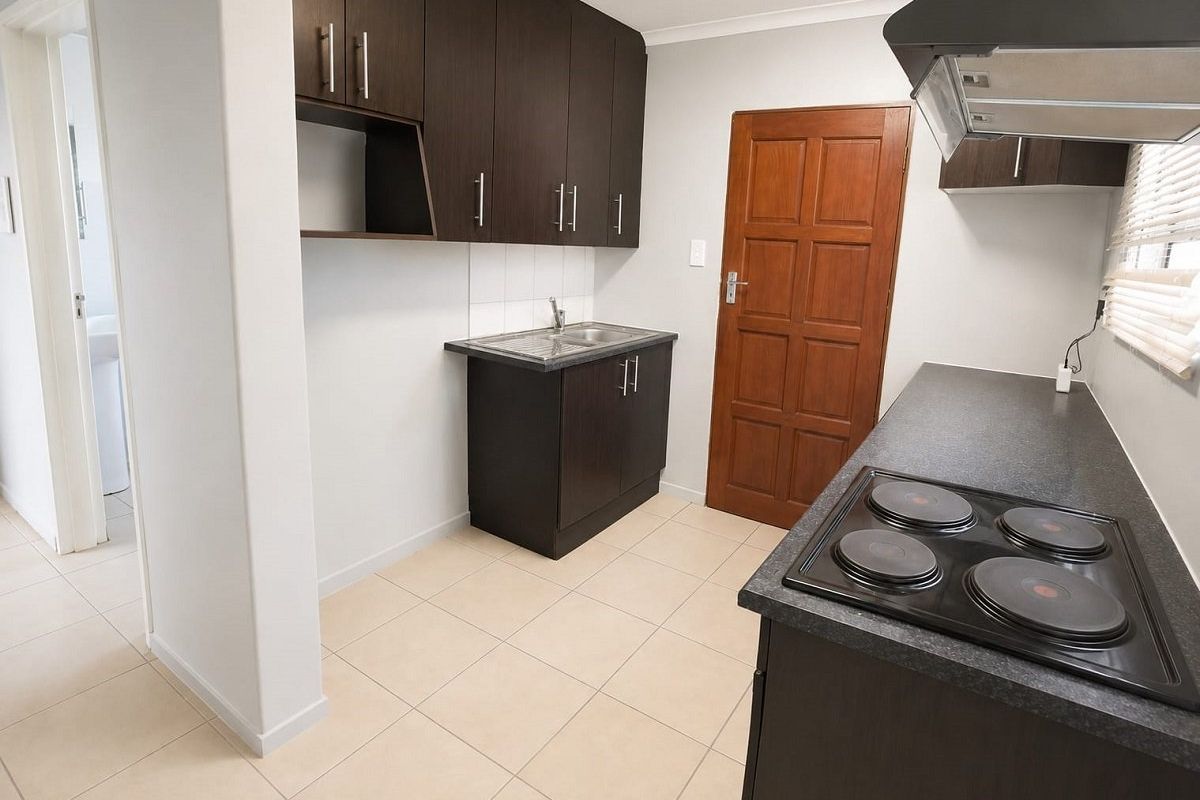A clean, functional kitchen featuring dark wood cabinetry, laminate countertops, an integrated electric hob with extractor fan, and neutral tiled flooring.
