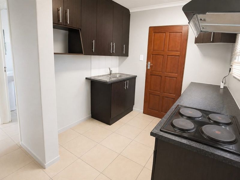 A clean, functional kitchen featuring dark wood cabinetry, laminate countertops, an integrated electric hob with extractor fan, and neutral tiled flooring.