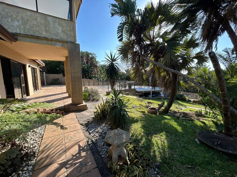 Rear exterior view featuring a tiled patio, concrete pillars, and a landscaped garden area with mature palm trees.