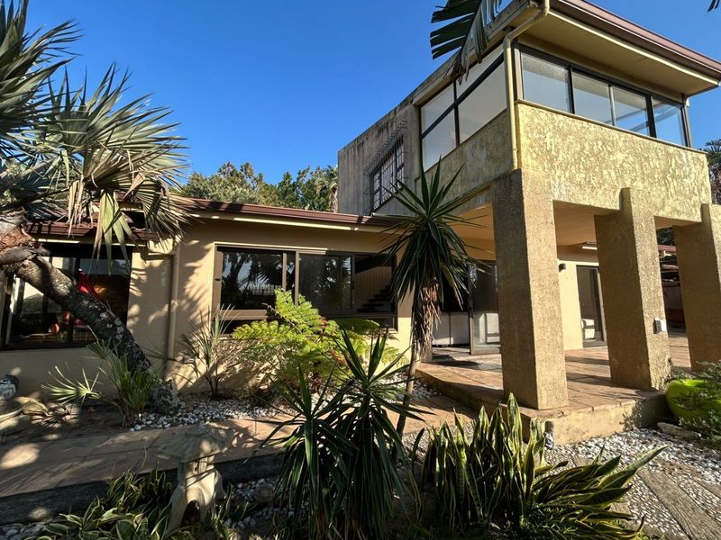 Rear view of the property featuring a tiled patio area, concrete structural pillars, and an upper-level balcony with aluminium window frames.