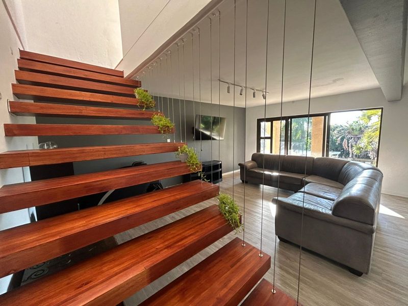 Modern living area featuring a striking floating timber staircase with cable balustrade, laminate flooring, and large sliding doors opening to the garden.