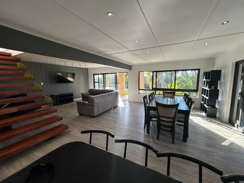 Spacious open-plan living and dining area featuring modern laminate flooring, a striking timber staircase, and large windows providing ample natural light.
