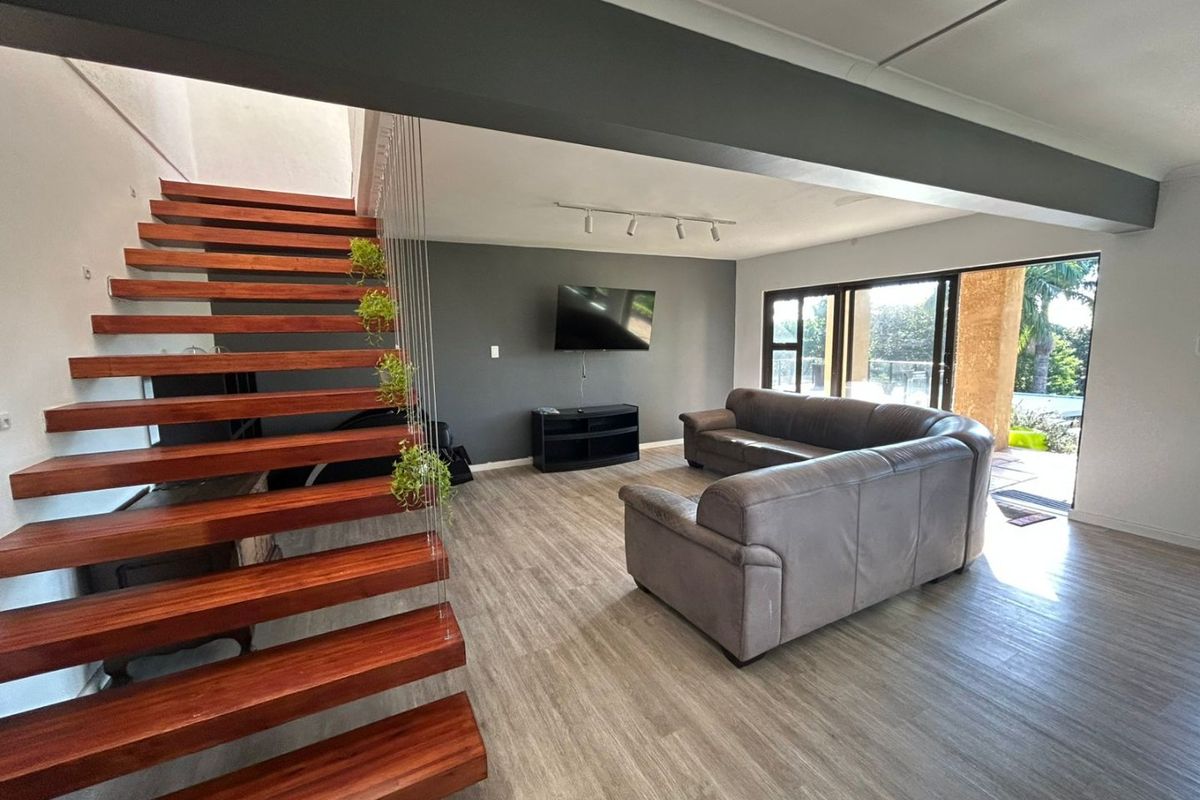 Spacious open-plan living area featuring a modern floating timber staircase, laminate flooring, and large sliding doors providing seamless access to the outdoor patio.