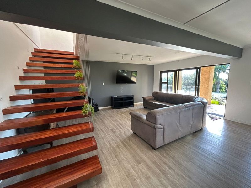 Spacious open-plan living area featuring a modern floating timber staircase, laminate flooring, and large sliding doors providing seamless access to the outdoor patio.