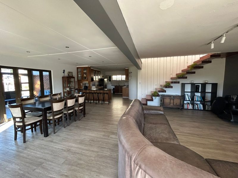 Spacious open-plan living, dining, and kitchen area featuring a modern wooden staircase, laminate flooring, and direct access to the outdoor patio.