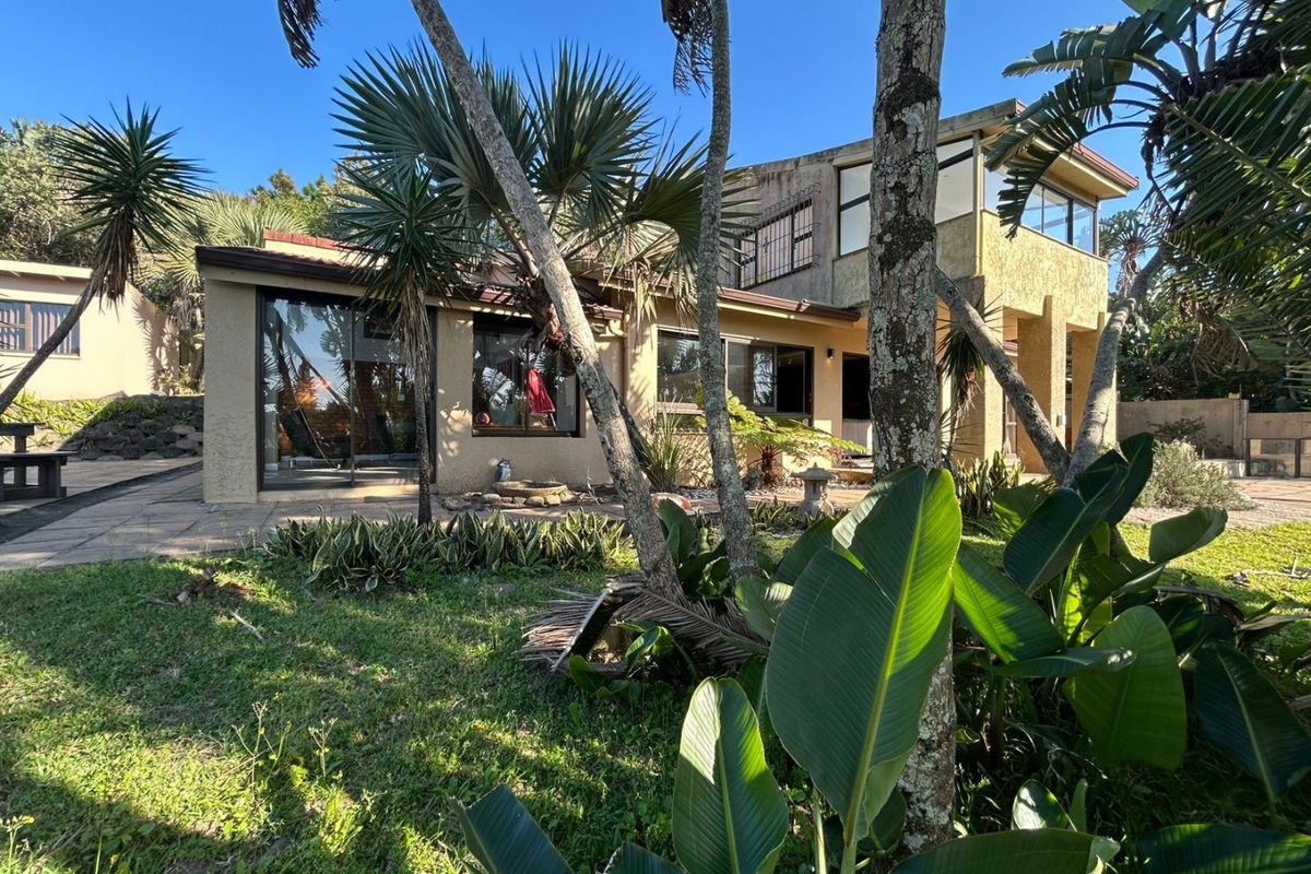 Rear view of the property featuring a paved patio area, sliding glass doors, and an upper-level balcony set within a landscaped garden.