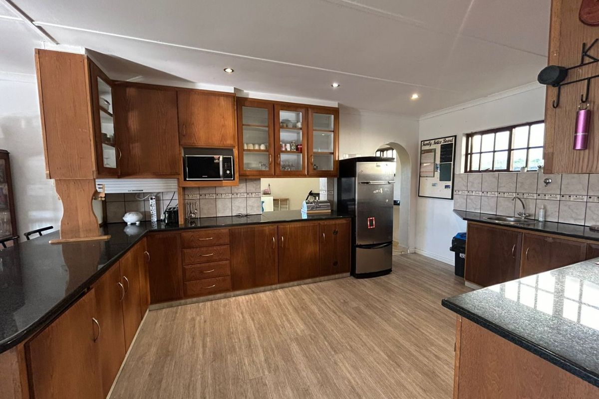 Spacious kitchen featuring extensive wooden cabinetry, dark granite countertops, tiled backsplash, and modern laminate flooring with integrated lighting.