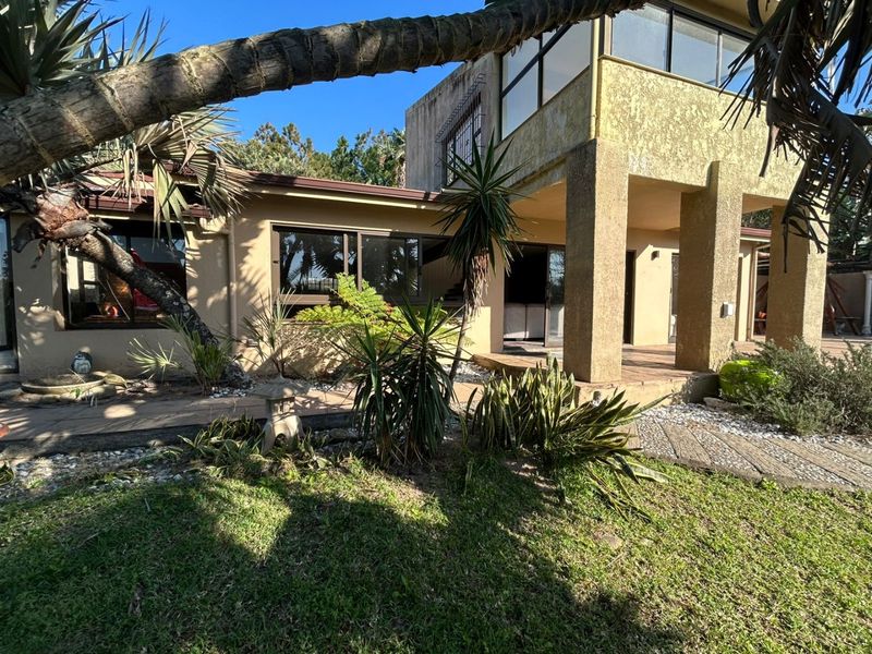 Rear view of the property featuring a covered patio area, sliding glass doors, and established garden landscaping with paved pathways.