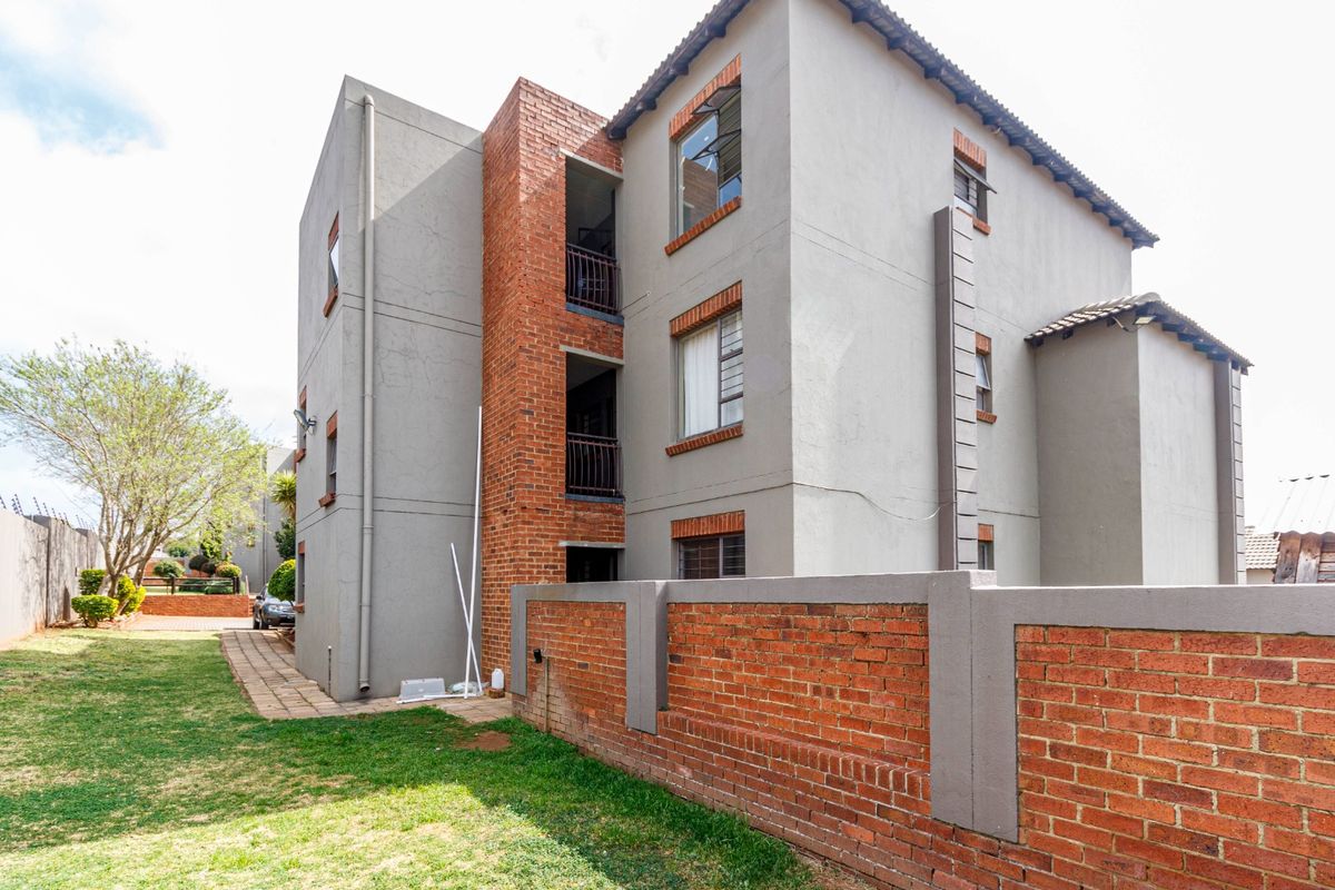 Rear view of a multi-story apartment building featuring brick and plaster facade, balconies, and a surrounding brick boundary wall.