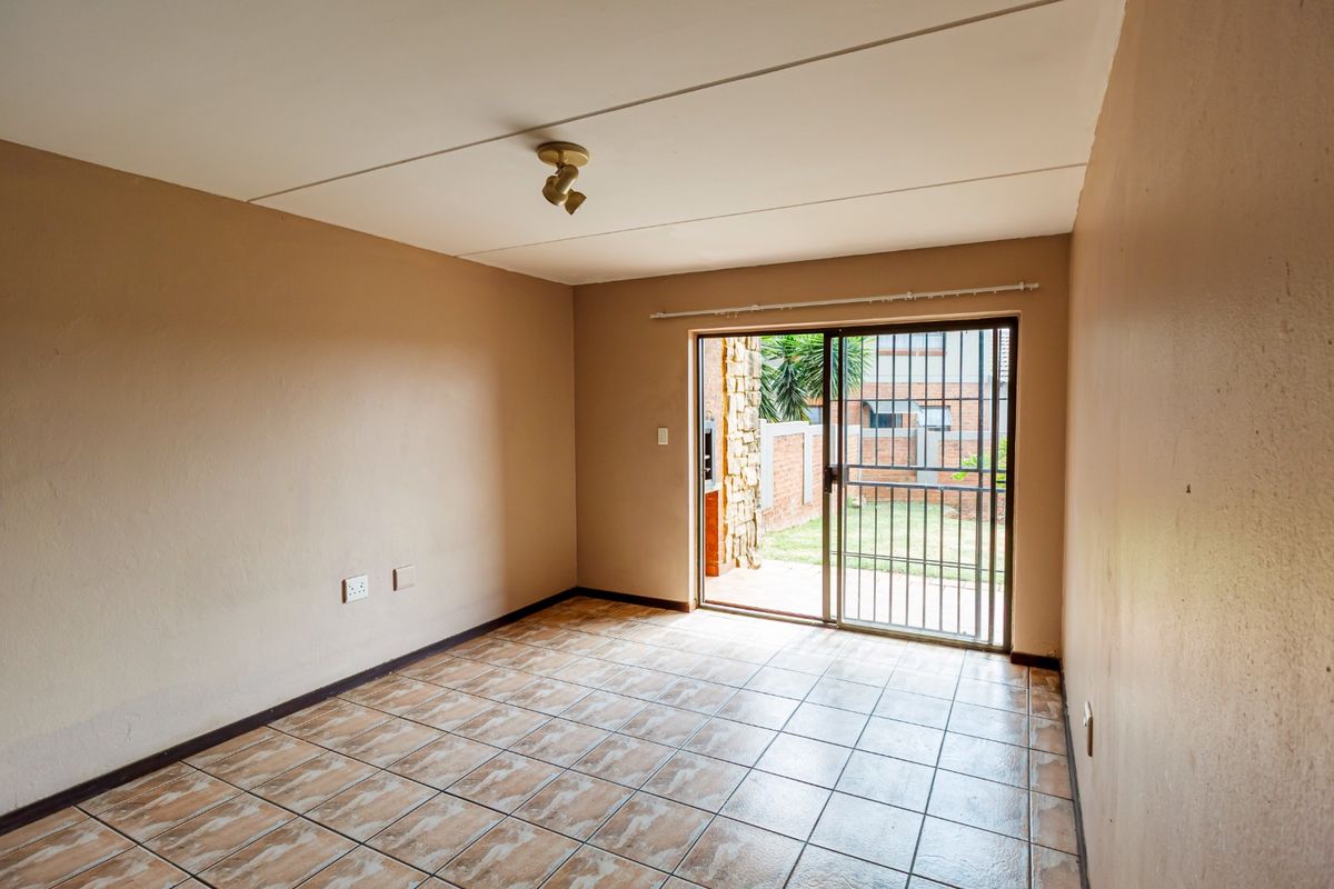 An empty living room featuring tiled flooring and a sliding glass door with a security gate, providing direct access to the outdoor area.