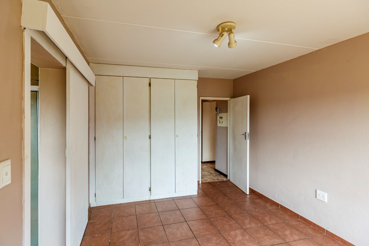 An empty bedroom featuring tiled flooring, built-in cupboards, and neutral wall tones, providing a blank canvas for personalization.