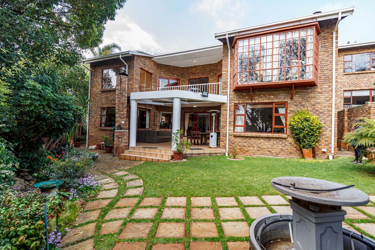 Rear view of a multi-story brick apartment building featuring a covered patio, balcony, bay window, and a landscaped garden with stone paving.
