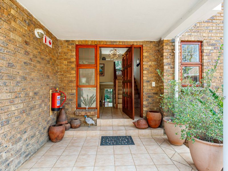 A welcoming covered entrance featuring face brick walls, tiled flooring, and a solid timber panelled door leading into the home.