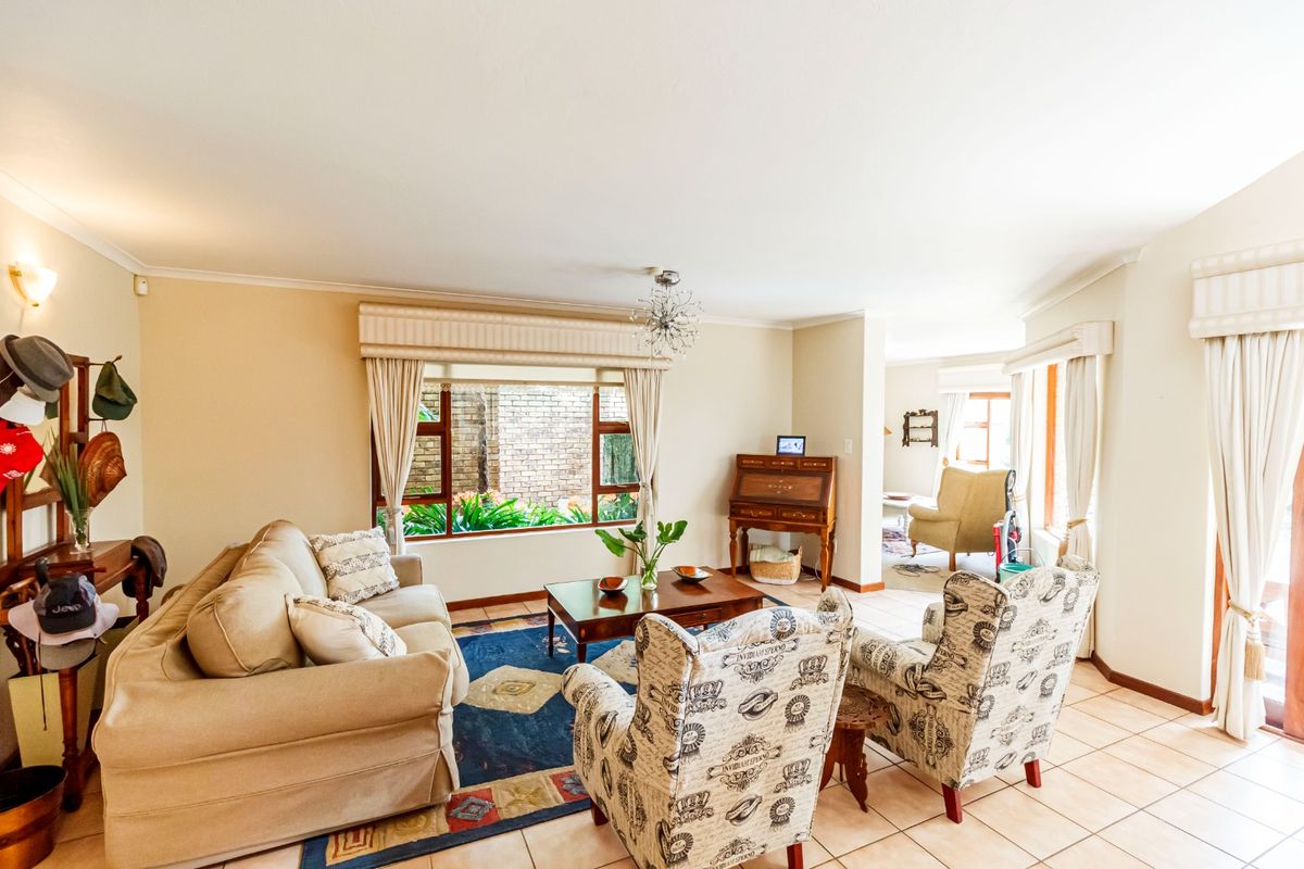A spacious living room featuring neutral tiled flooring, large windows with built-in pelmets, and a bright, open layout connecting to adjacent living areas.