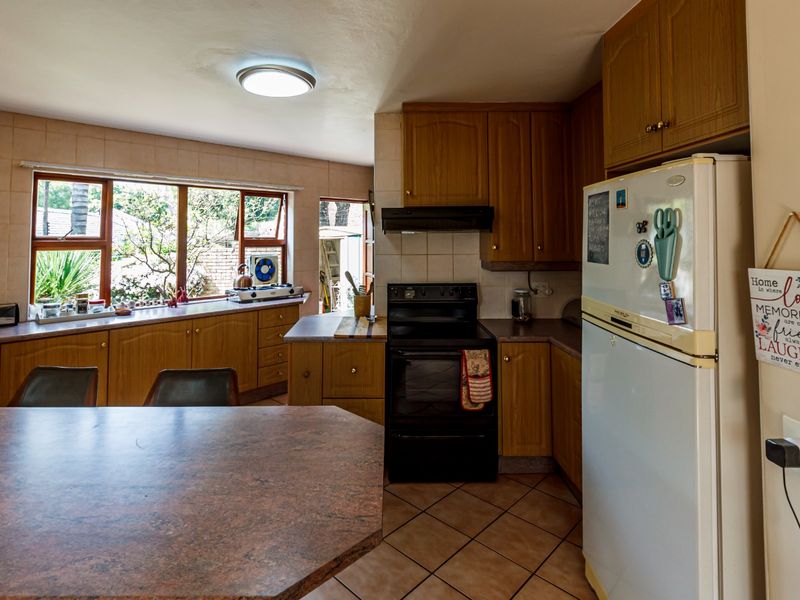 A functional kitchen featuring wooden cabinetry, laminate countertops, tiled flooring, and a built-in oven with an extractor fan, overlooking a garden area.