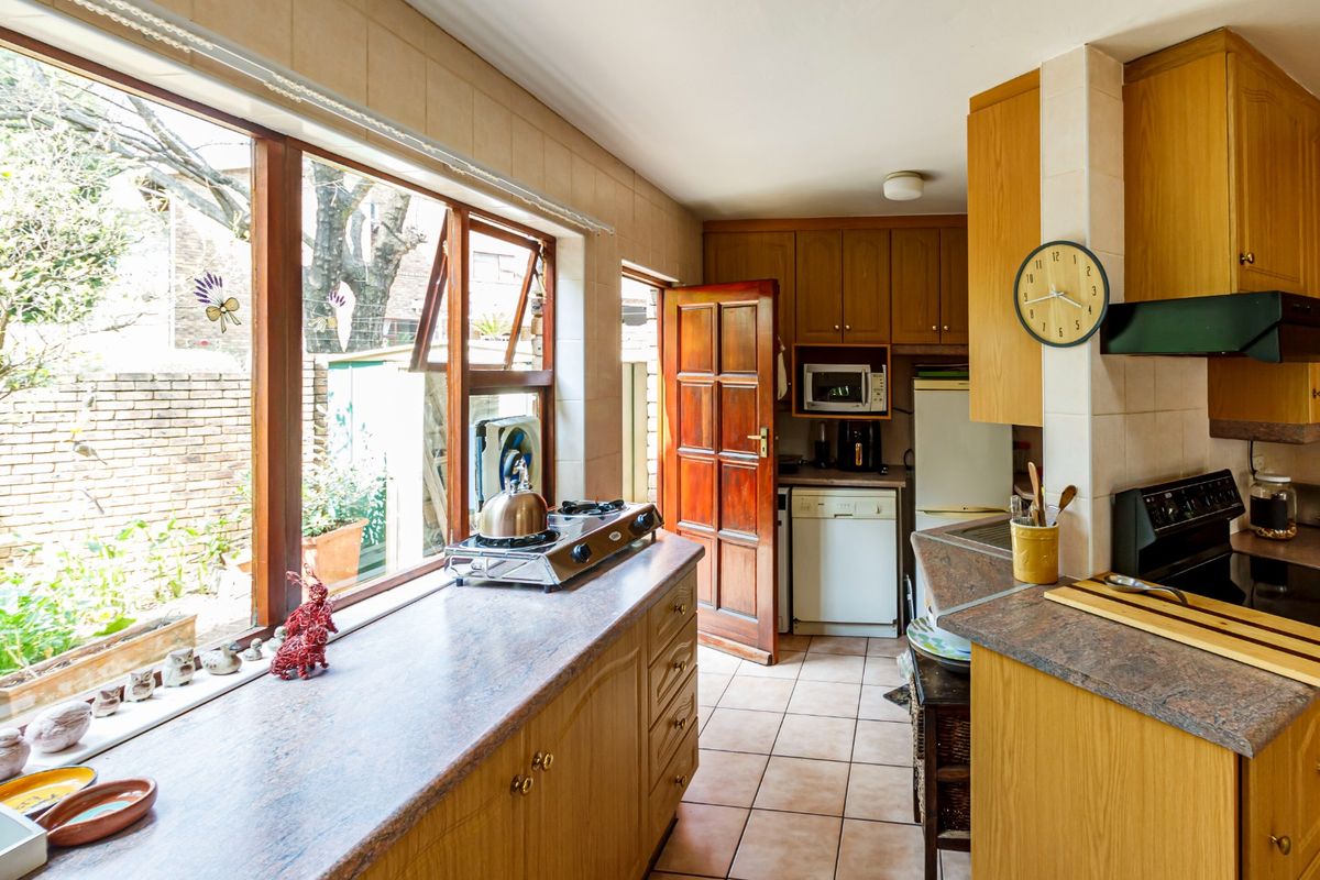 A functional kitchen featuring wooden cabinetry, laminate countertops, tiled flooring, and a large window providing natural light and garden views.