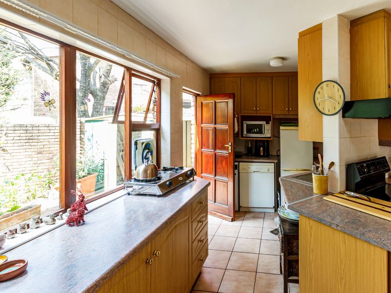A functional kitchen featuring wooden cabinetry, laminate countertops, tiled flooring, and a large window providing natural light and garden views.
