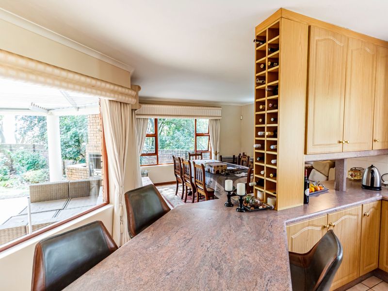 Open-plan kitchen and dining area featuring built-in cabinetry, a dedicated wine rack, and a breakfast bar overlooking the outdoor patio and garden.