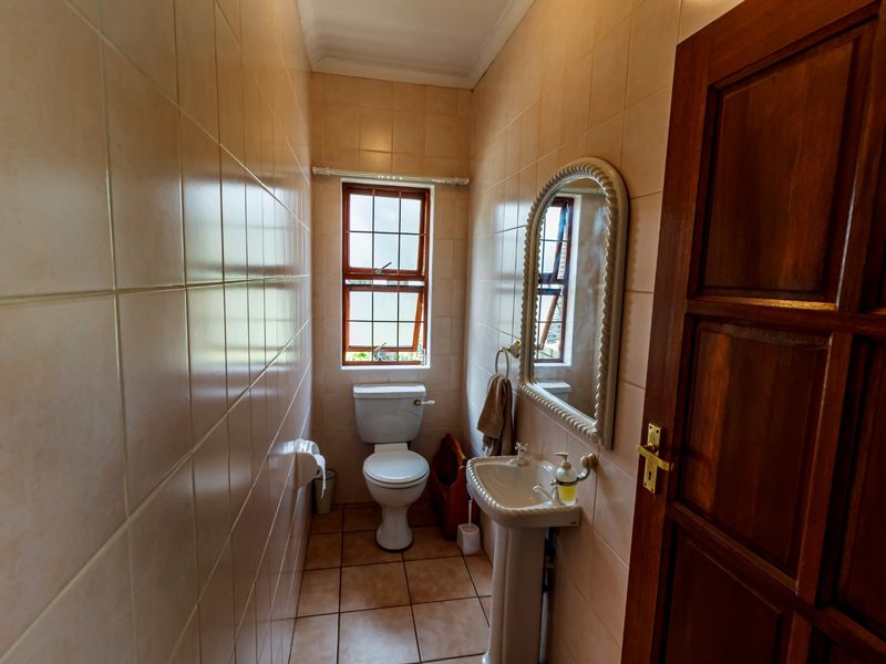 A compact bathroom featuring tiled walls and flooring, a pedestal basin, and a toilet, with natural light provided by a small casement window.