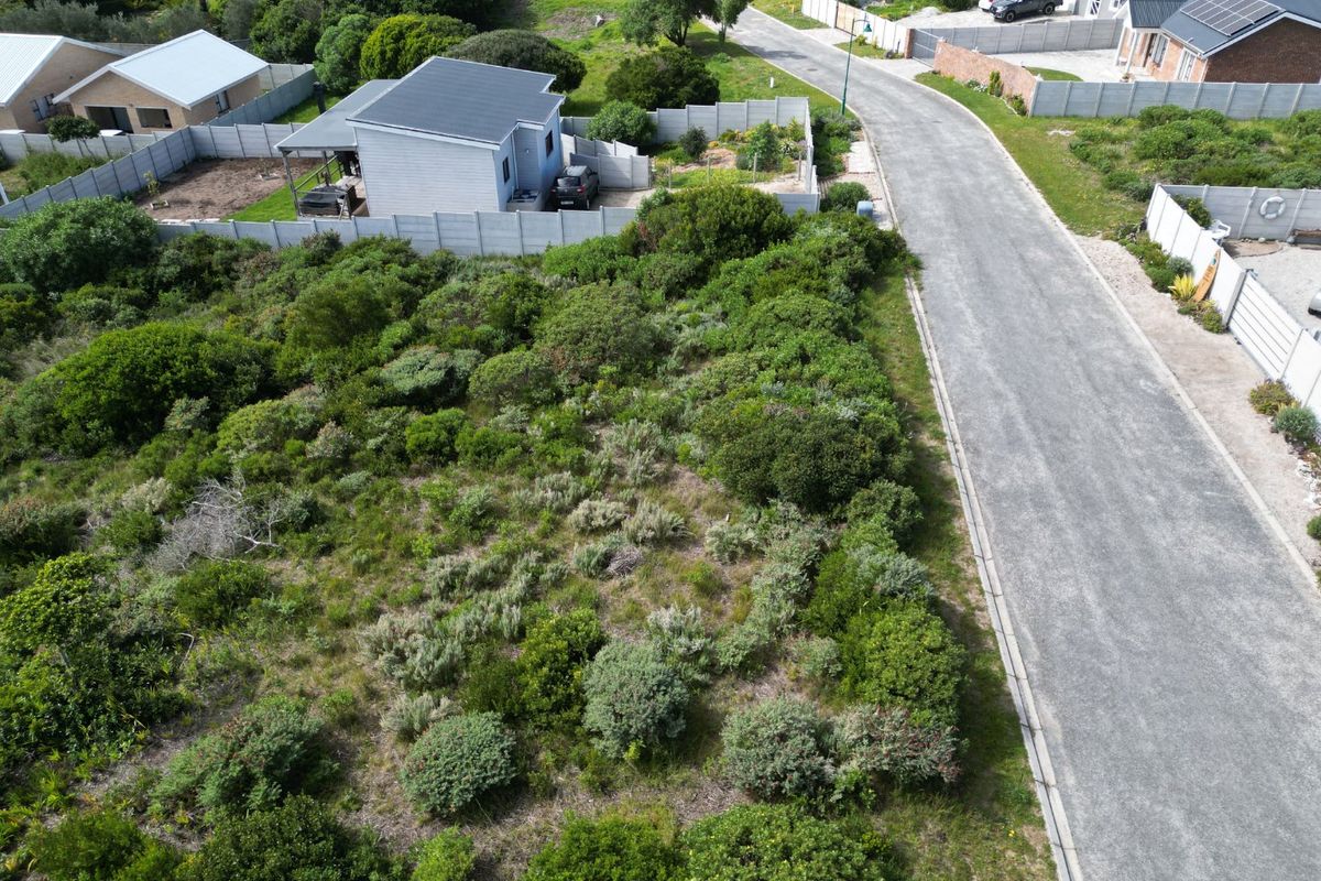 Aerial view of a vacant residential plot featuring natural vegetation, adjacent to a paved road and established residential properties.