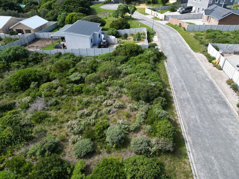 Aerial view of a vacant residential plot featuring natural vegetation, adjacent to a paved road and established residential properties.