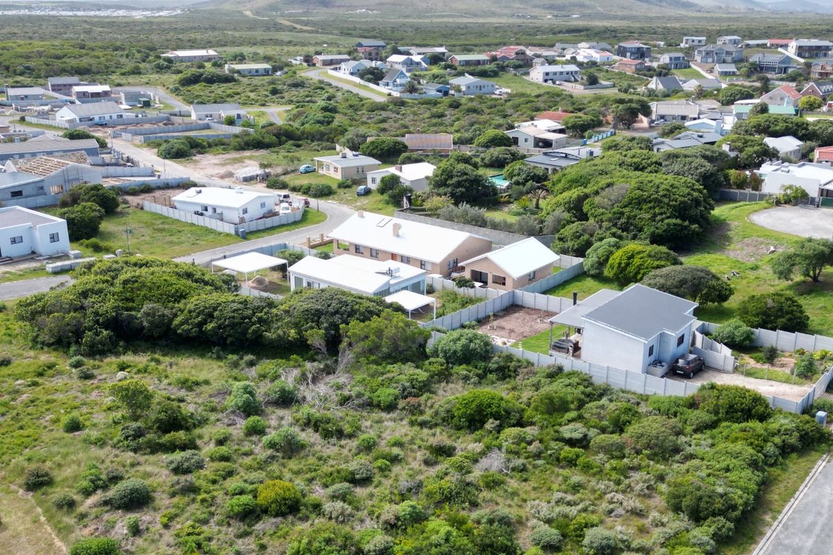 An aerial view of a residential neighborhood featuring established homes, fenced plots, and surrounding coastal landscape.