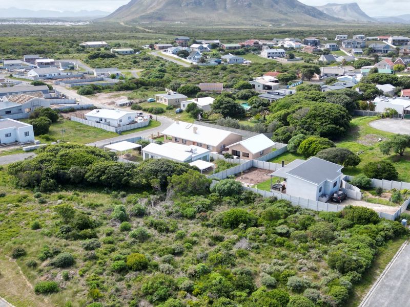 An aerial view of a residential neighborhood featuring established homes, fenced plots, and surrounding coastal landscape.