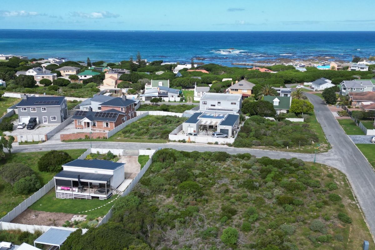 Aerial view of a coastal residential neighborhood featuring a vacant land plot in the foreground with ocean views in the distance.