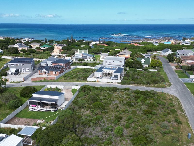 Aerial view of a coastal residential neighborhood featuring a vacant land plot in the foreground with ocean views in the distance.
