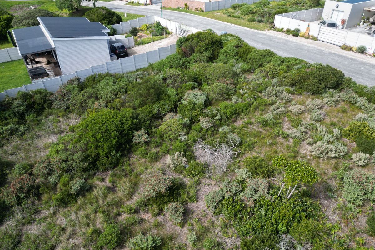 An aerial view of a vacant residential plot featuring natural vegetation, enclosed by a precast concrete boundary wall with adjacent road access.
