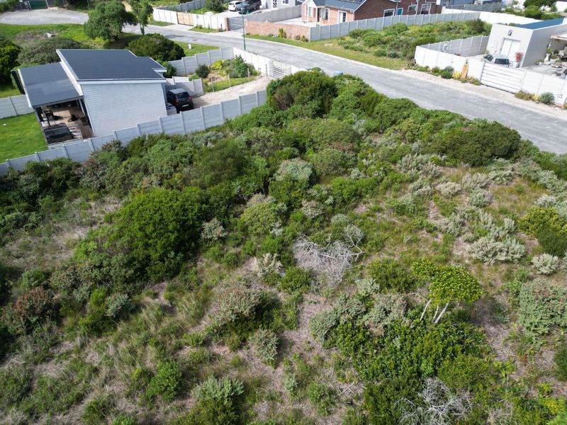 An aerial view of a vacant residential plot featuring natural vegetation, enclosed by a precast concrete boundary wall with adjacent road access.