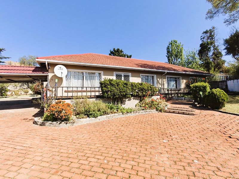 Front view of a single-story house featuring a tiled roof, brick paved driveway, and an attached carport with established garden beds.