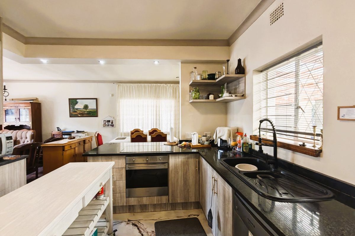 A functional kitchen featuring wood-look cabinetry, dark granite countertops, a built-in oven, and a double sink, seamlessly flowing into the adjacent living area.