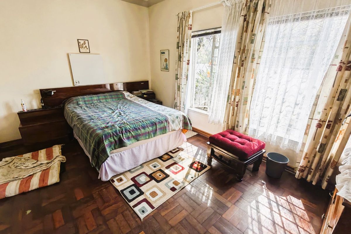 A bedroom featuring classic parquet flooring, a built-in wooden headboard, and large windows with security bars allowing for natural light.