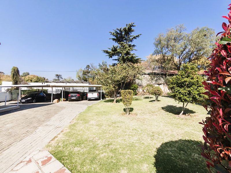 A well-maintained front exterior featuring a paved driveway, a functional carport for multiple vehicles, and a neat, established garden area.