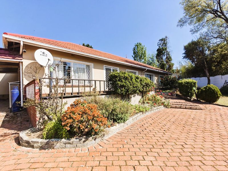 Rear view of the house featuring a tiled roof, raised patio area, and a brick-paved courtyard with established garden beds.
