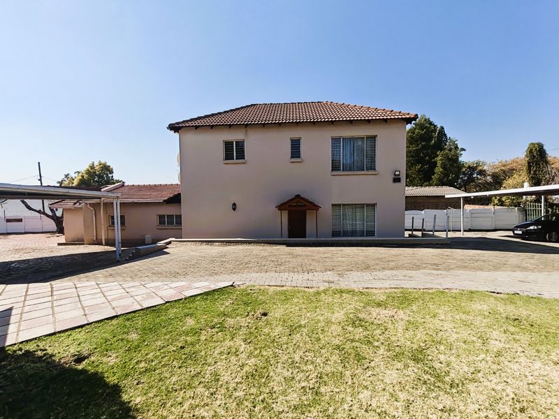 Front view of a two-story residential house featuring a paved driveway, carport, and established lawn area.