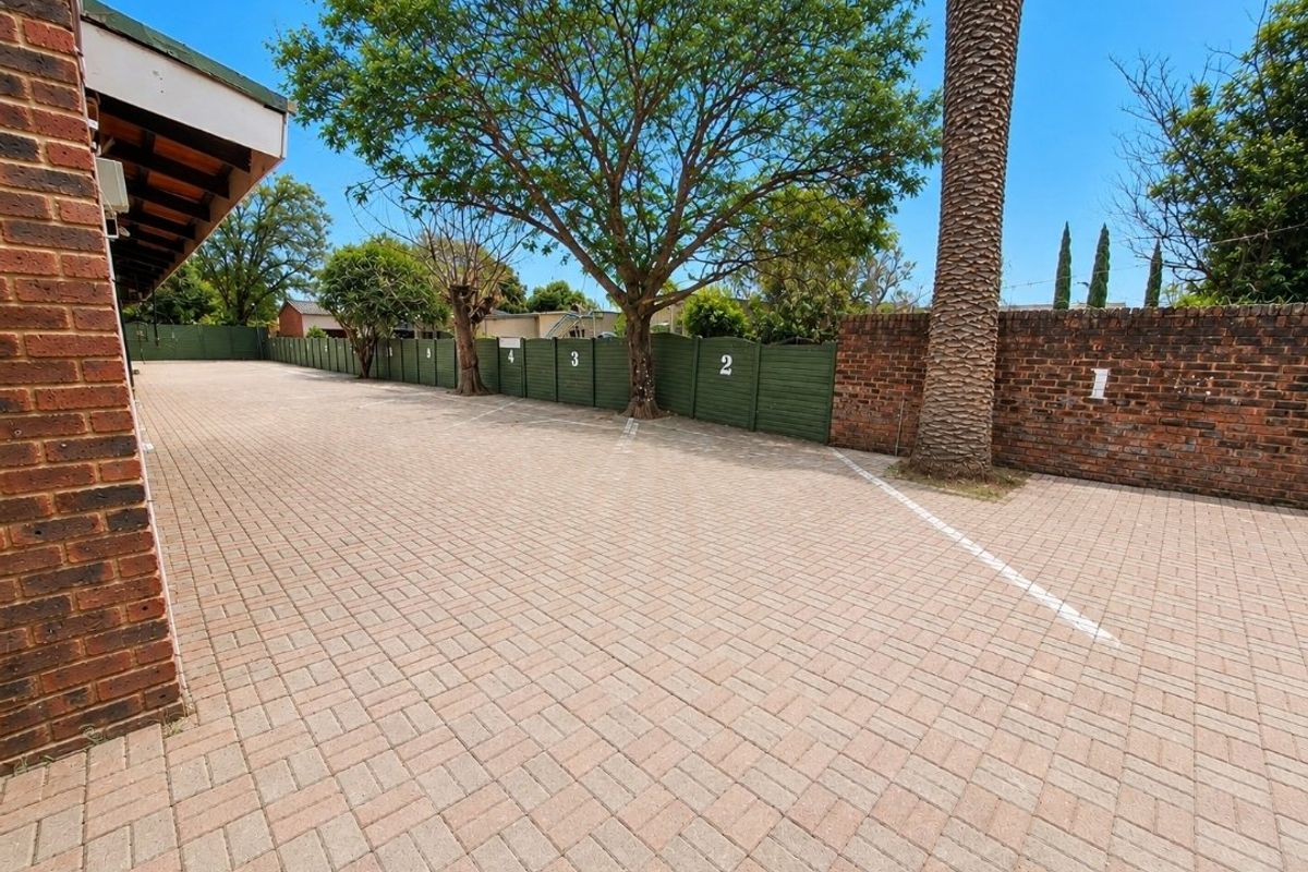 A well-maintained paved parking area featuring numbered bays, brick boundary walls, and established trees, providing secure and organized commercial parking space.