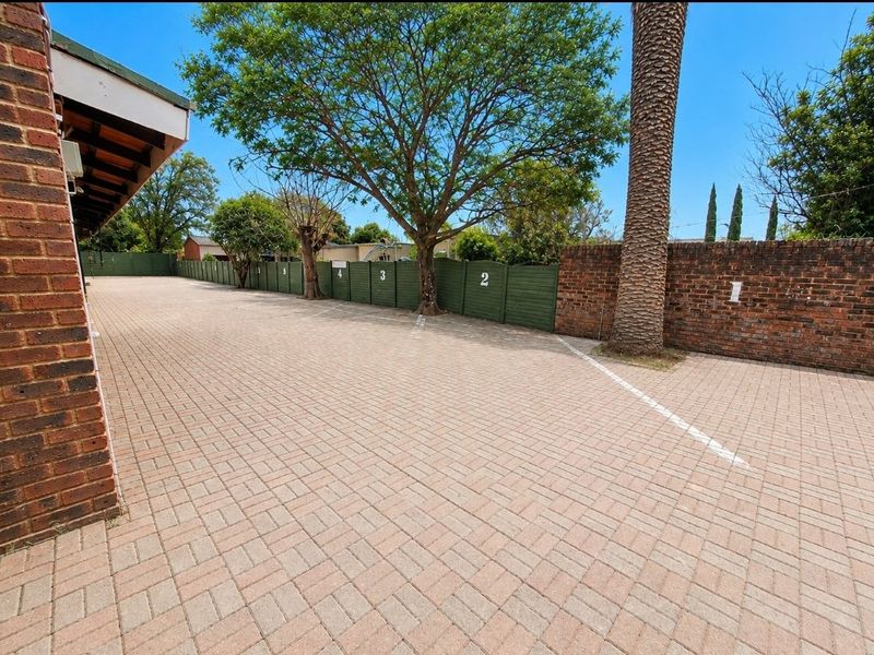 A well-maintained paved parking area featuring numbered bays, brick boundary walls, and established trees, providing secure and organized commercial parking space.