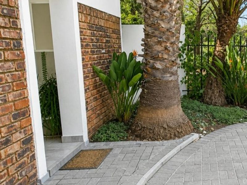 A well-maintained commercial building entrance featuring a brick facade, paved driveway, and established palm tree landscaping.