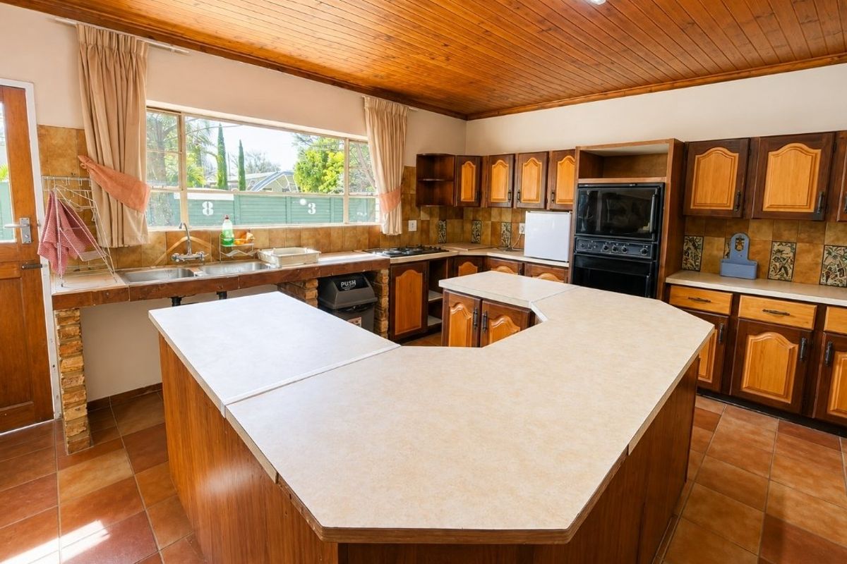 Spacious kitchen featuring extensive wooden cabinetry, laminate countertops, a built-in oven, and a distinctive timber ceiling with tiled flooring.