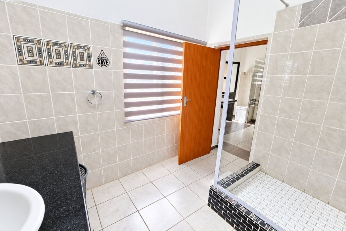 A clean, modern bathroom featuring a granite-topped vanity, tiled walk-in shower with glass enclosure, and neutral ceramic finishes throughout.